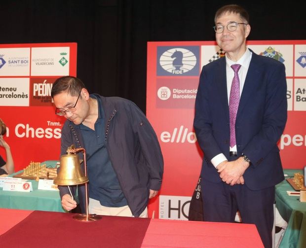 El doctor Yi Ling, socio fundador de la asesoría Linkchina, realizando el tradicional toque de campana que da inicio a las partidas del Llobregat Open Chess Tournament, acompañado de Jorge I. Aguadero Casado, jefe de redacción de Peón de Rey.